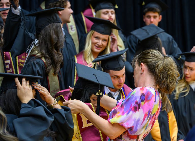 A faculty or staff member helps graduates adjust ceremonial stoles before Elon University’s Graduate Commencement ceremony.