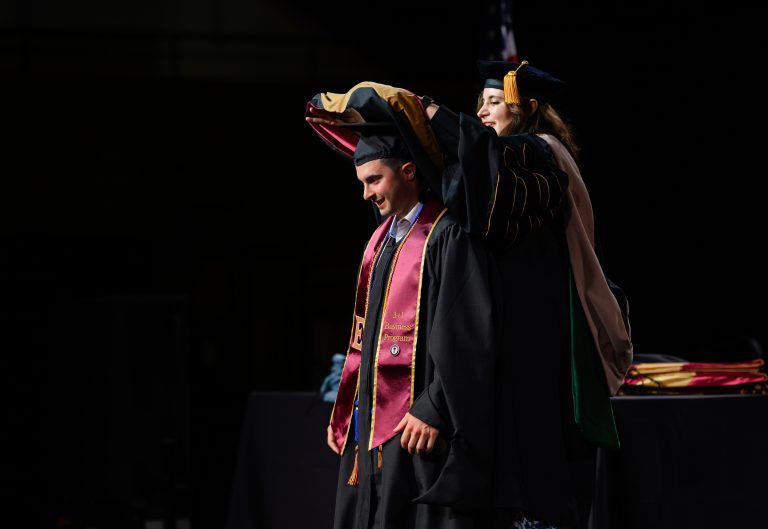 A faculty member places a doctoral hood over a graduate during Elon University’s Graduate Commencement ceremony.