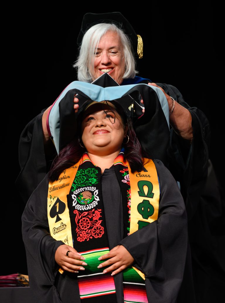 A faculty member places a hood on a graduate wearing colorful honor stoles during Graduate Commencement.