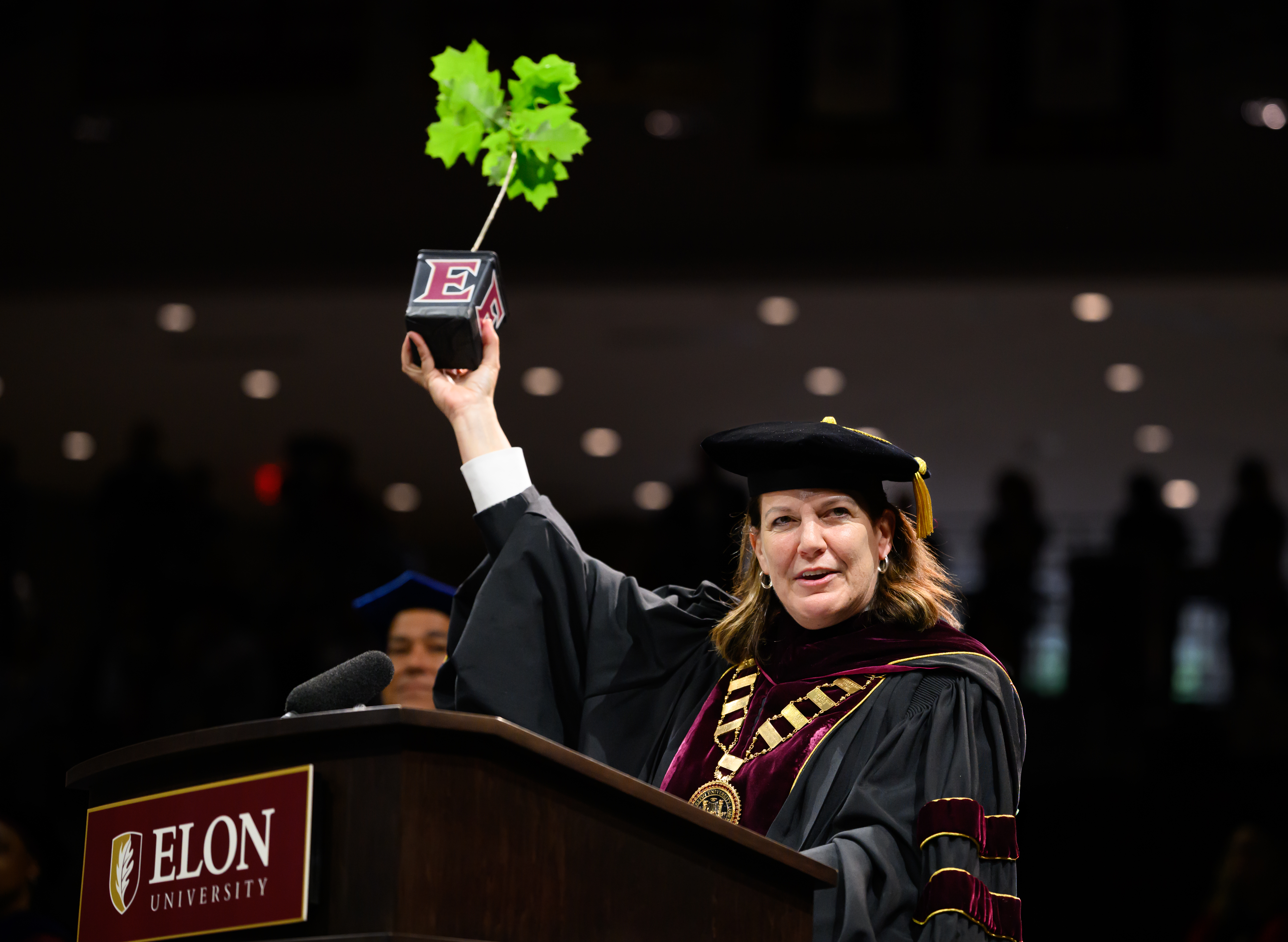 University president holds up a small oak sapling at the podium during Elon University commencement ceremony.