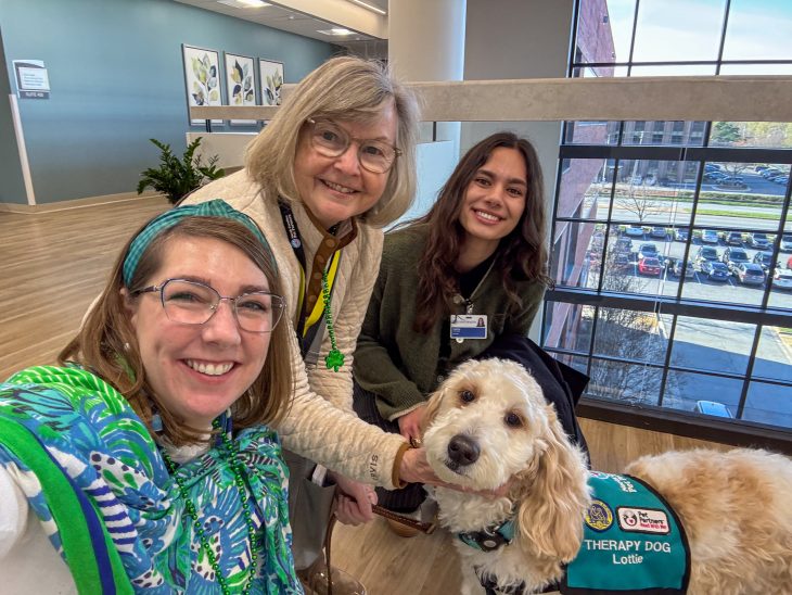 Simrin Carlsen G’26 poses with two people and Lottie, a therapy dog, inside a Cone Health building.