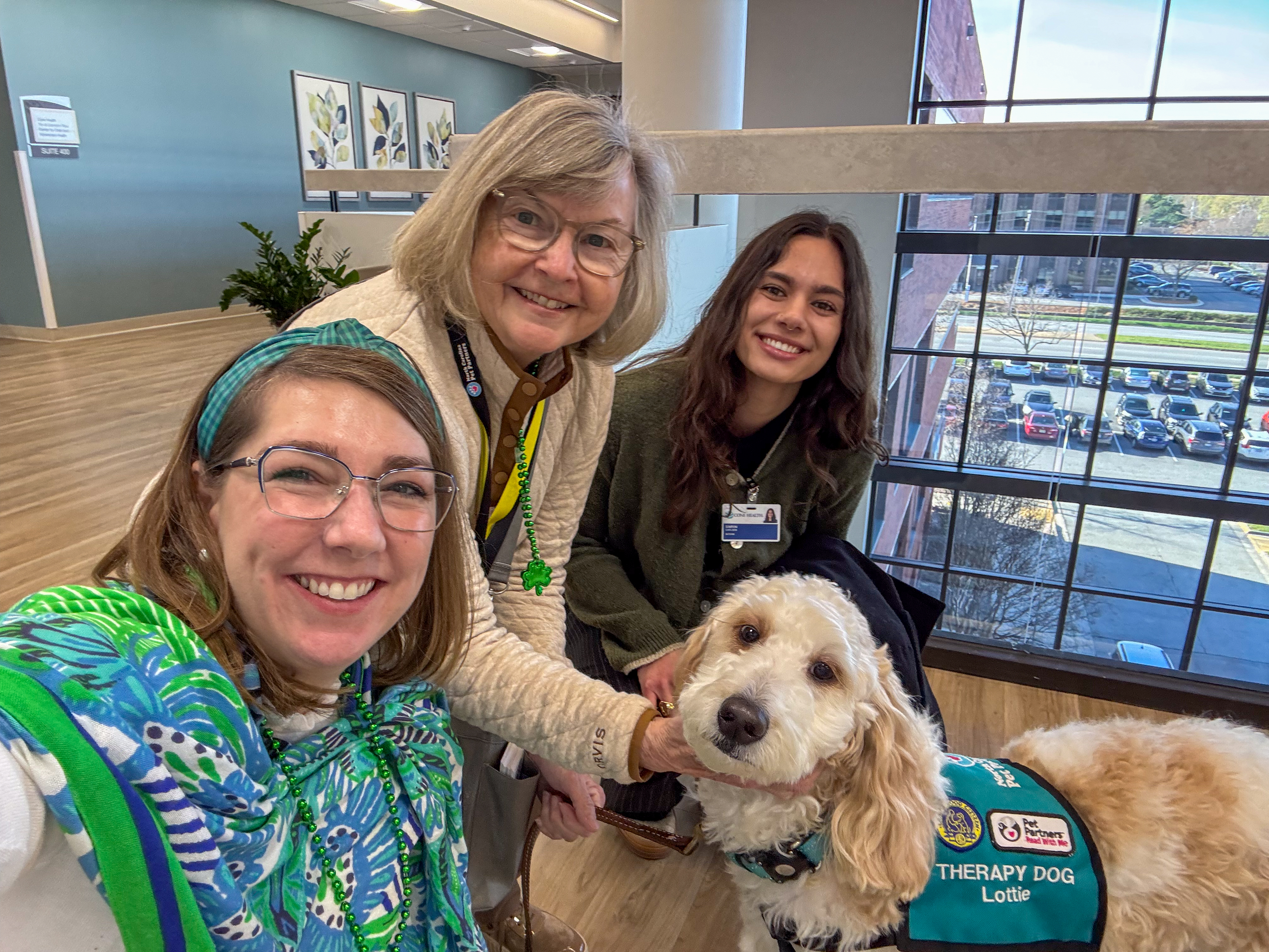 Simrin Carlsen G’26 poses with two people and Lottie, a therapy dog, inside a Cone Health building.