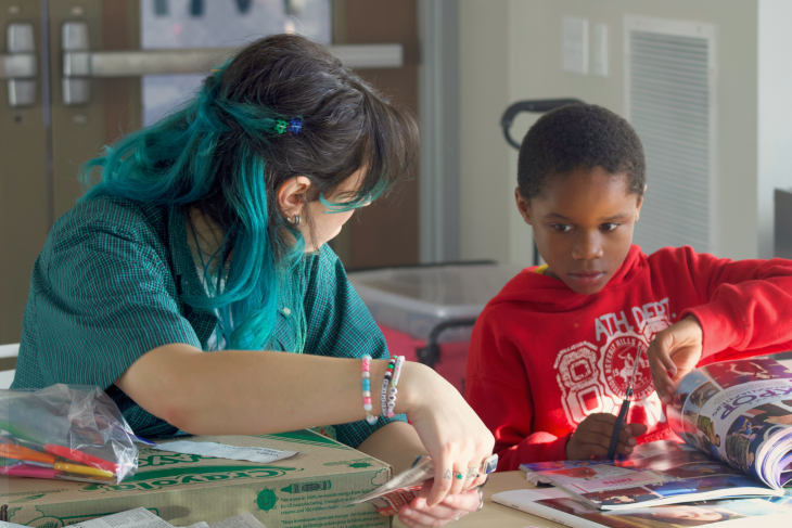 A volunteer assists a student with collaging at a session