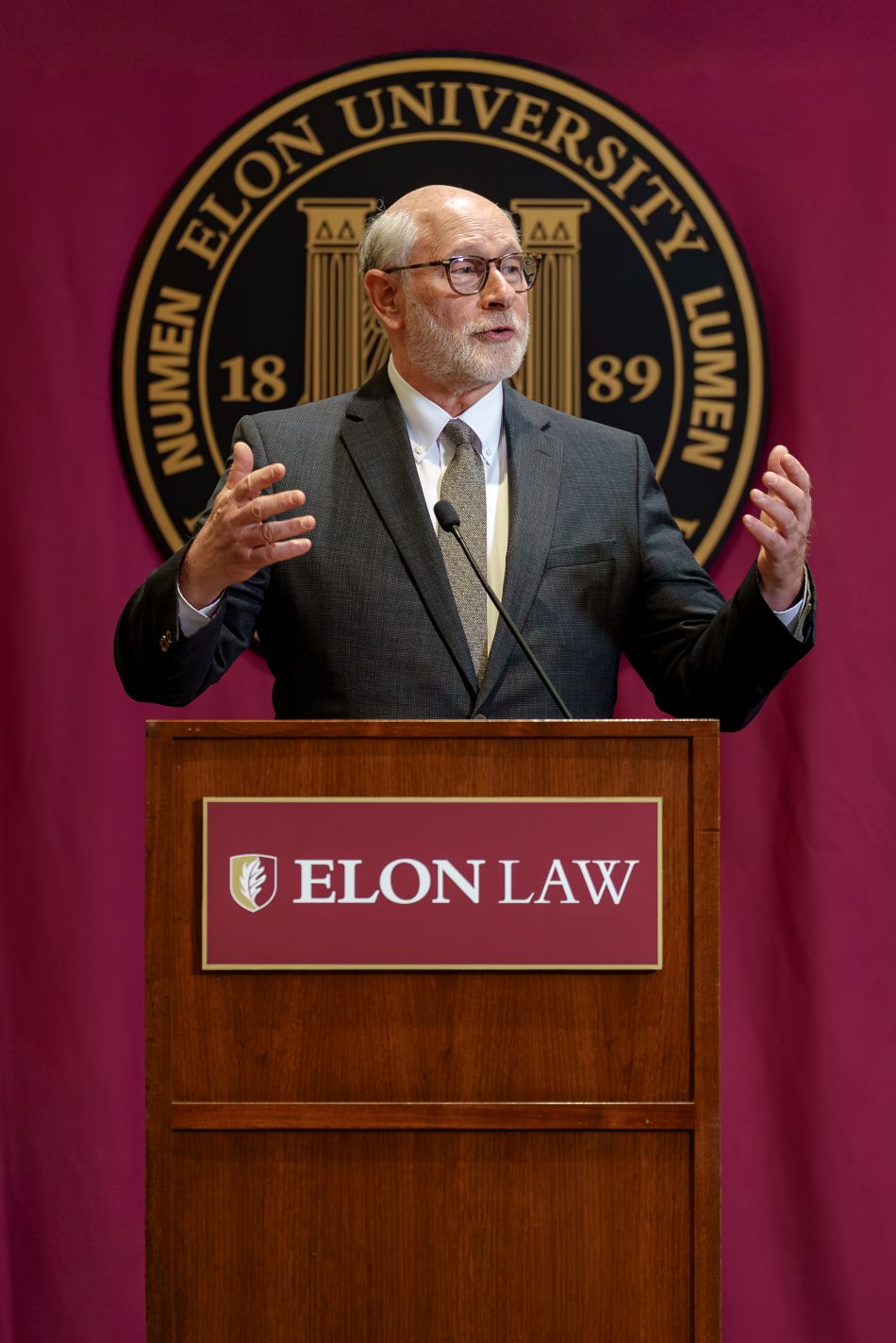 Luke Bierman in a suit on a stage with the ELon University seal and behind an Elon Law podium.