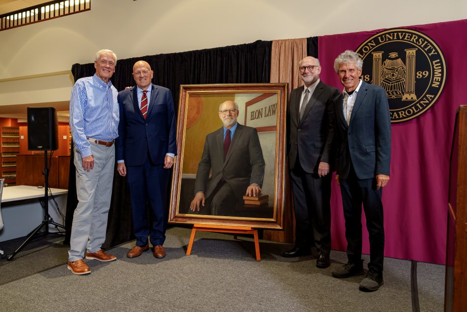 Four men stand smiling around a painted portrait of Dean Emeritus Luke Bierman