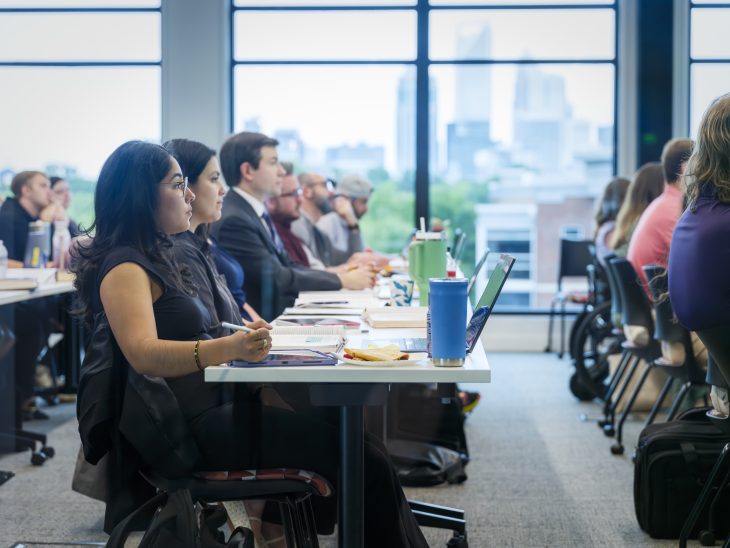 A group of law students seated at long desks in a classroom overlooking the Charlotte skyline.