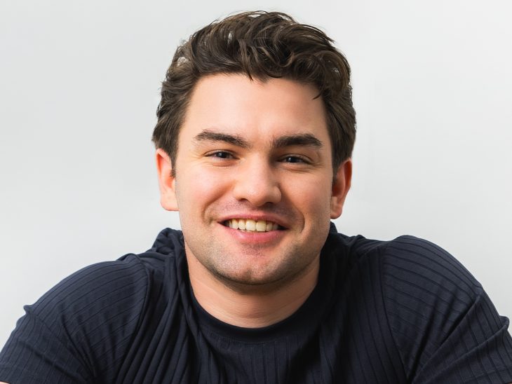 A man in a black shirt poses for a photo on a white background smiling