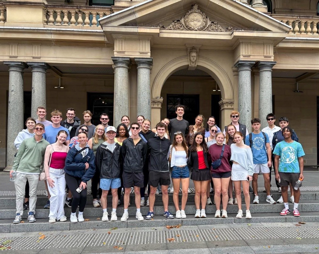 Group of Elon University Business Fellows posing together on the steps outside a historic sandstone building with columns in Sydney.