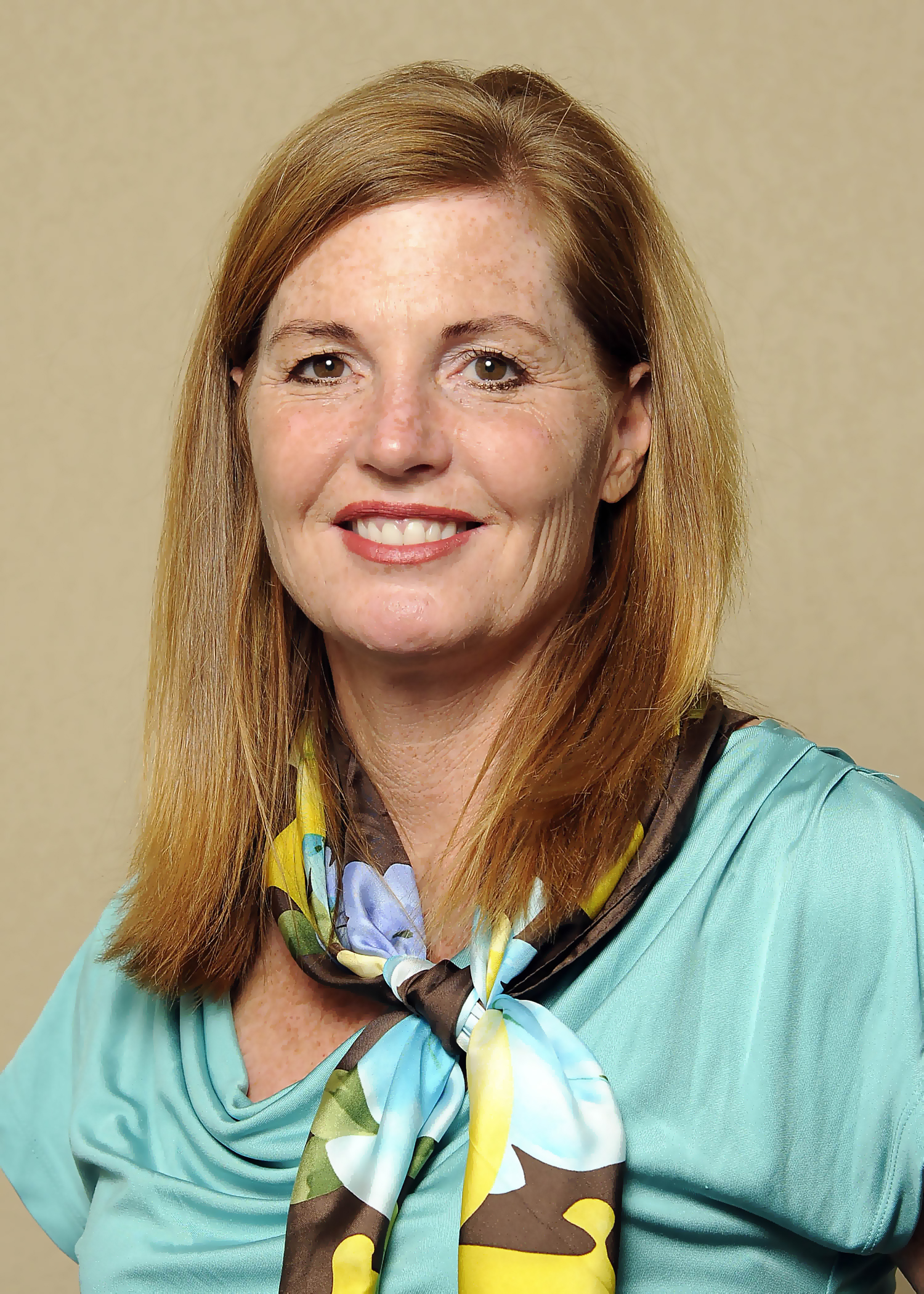 A formal portrait of Anne Powell wearing a blue top and multicolored scarf