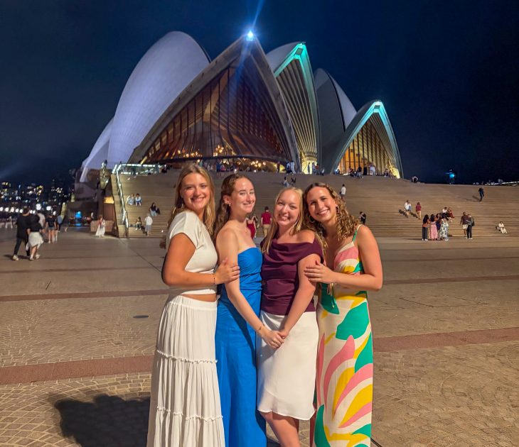 Four Business Fellows pose together at night in front of the illuminated Sydney Opera House during the Asia Pacific semester experience.