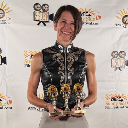 Ashley Christman holds up three awards against festival backdrop