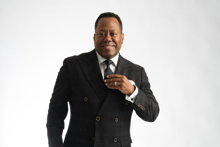 Studio portrait of Nick Cooper wearing a white dress shirt and black textured vest against a dark background.