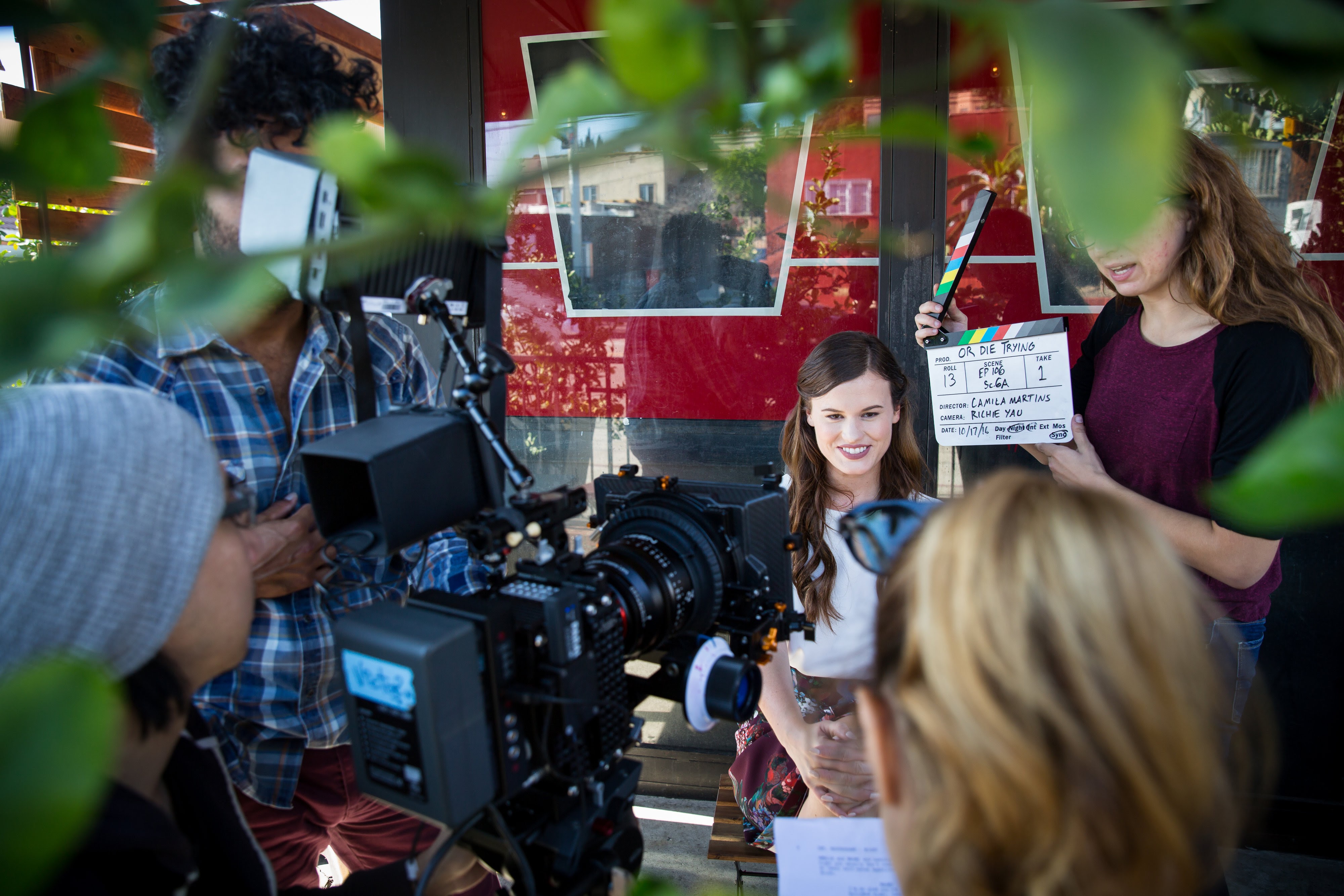 People film a scene on a movie set, operating a professional camera while a crew member holds a clapperboard and an actor prepares for a take.