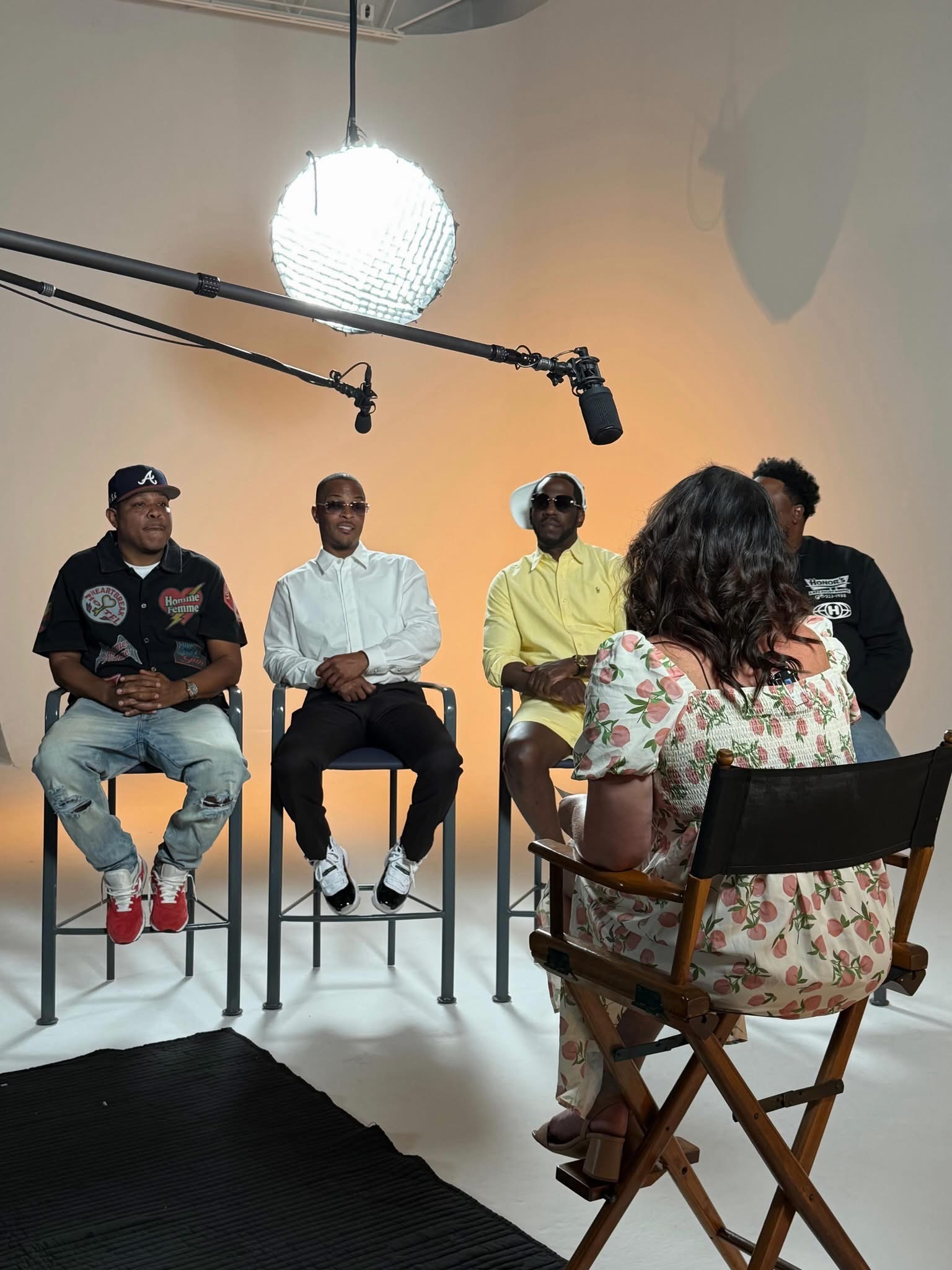 An interviewer speaks with four seated participants in a professional studio, with microphones and lighting equipment visible during a recorded discussion.