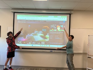 Two male students standing in front of screen showing the game they built.