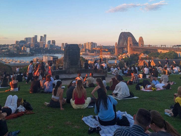 People sit on a grassy overlook at sunset with the Sydney Harbour Bridge, city skyline and water in the background during the Business Fellows’ Asia Pacific semester experience.