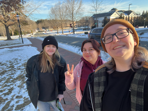 Three students smiling on a snowy campus walkway on a sunny winter day, one flashing a peace sign.