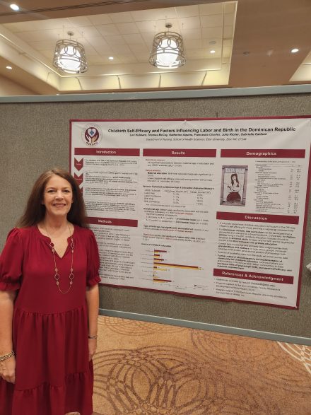 A person in a red dress poses for a photo in front of a research poster 