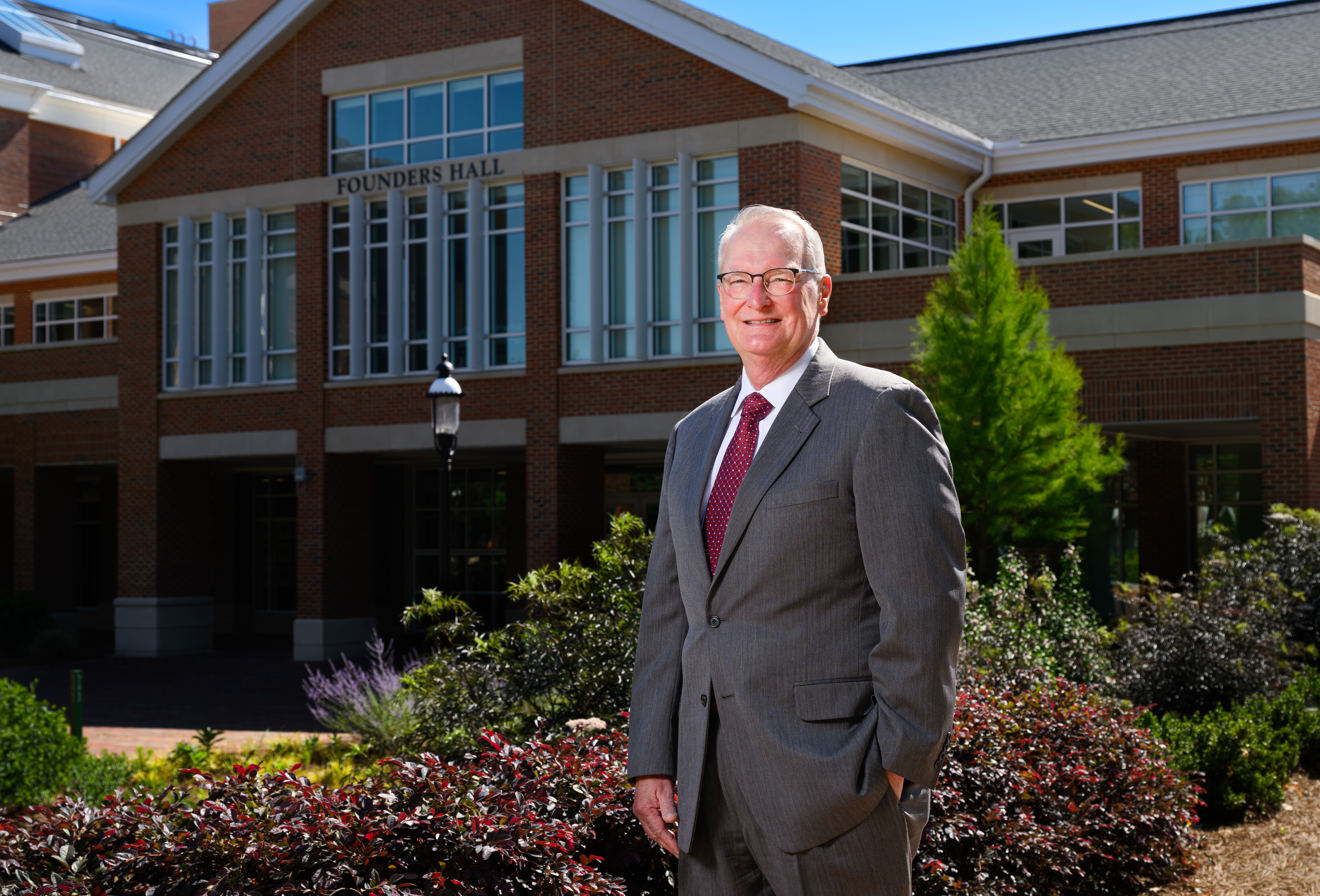 A man in a suit stands in front of a brick building in a portrait photo