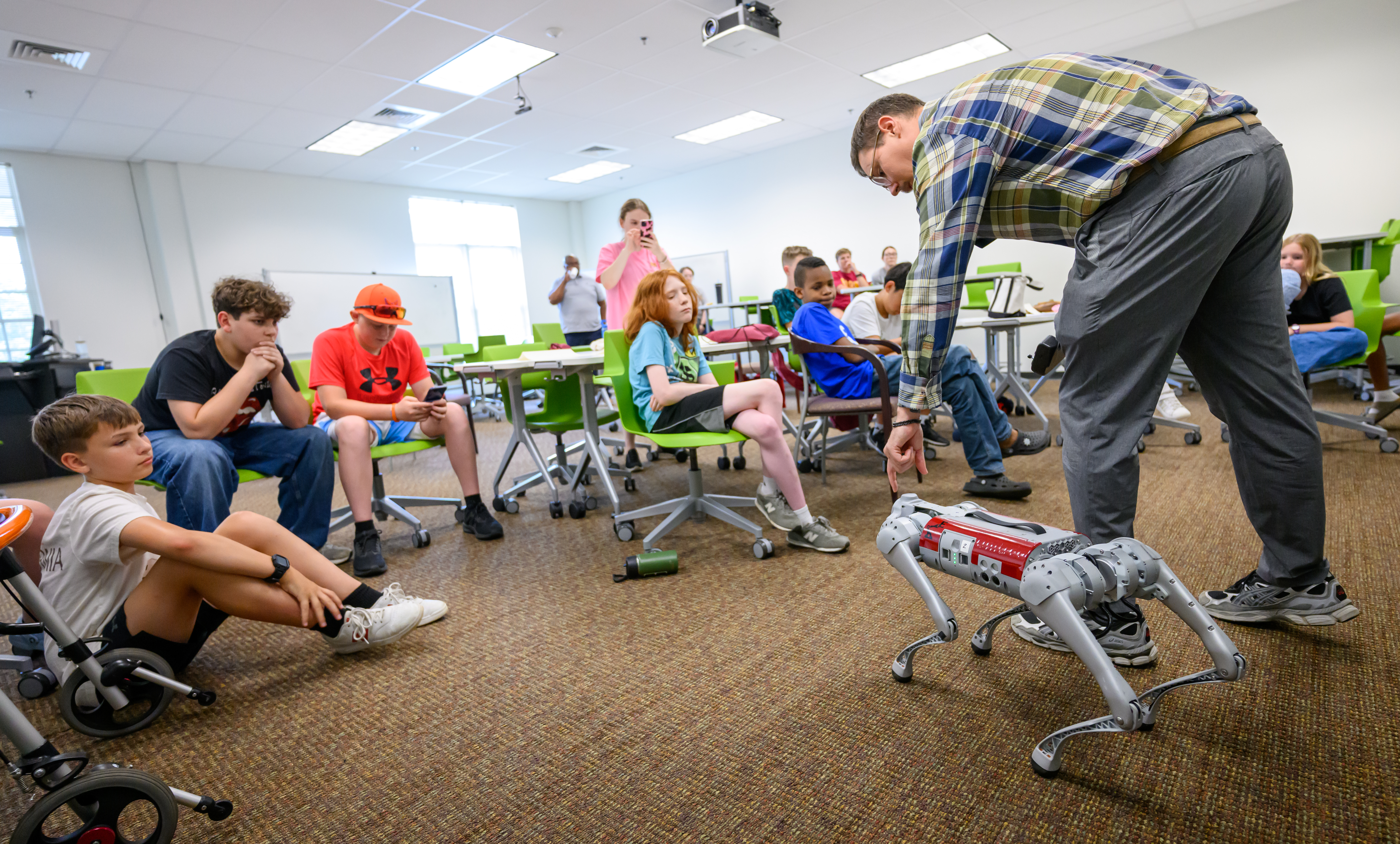 An instructor demonstrates a four-legged robotic dog to children attending a summer technology camp as participants watch and learn about robotics and artificial intelligence.