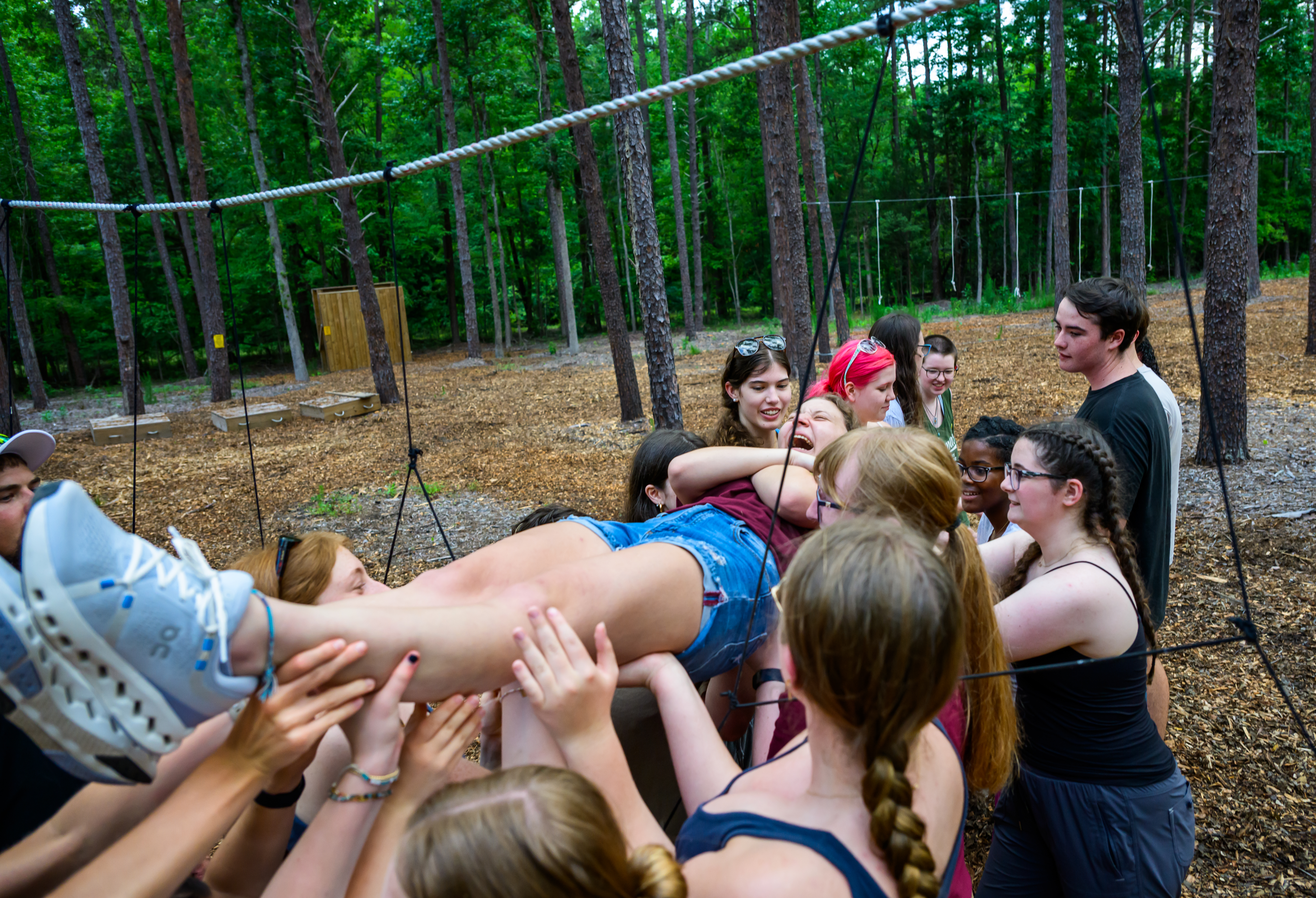 Students work together to support a classmate through a team-building challenge on the 51������ ropes course, lifting the participant across suspended ropes during an outdoor leadership exercise.