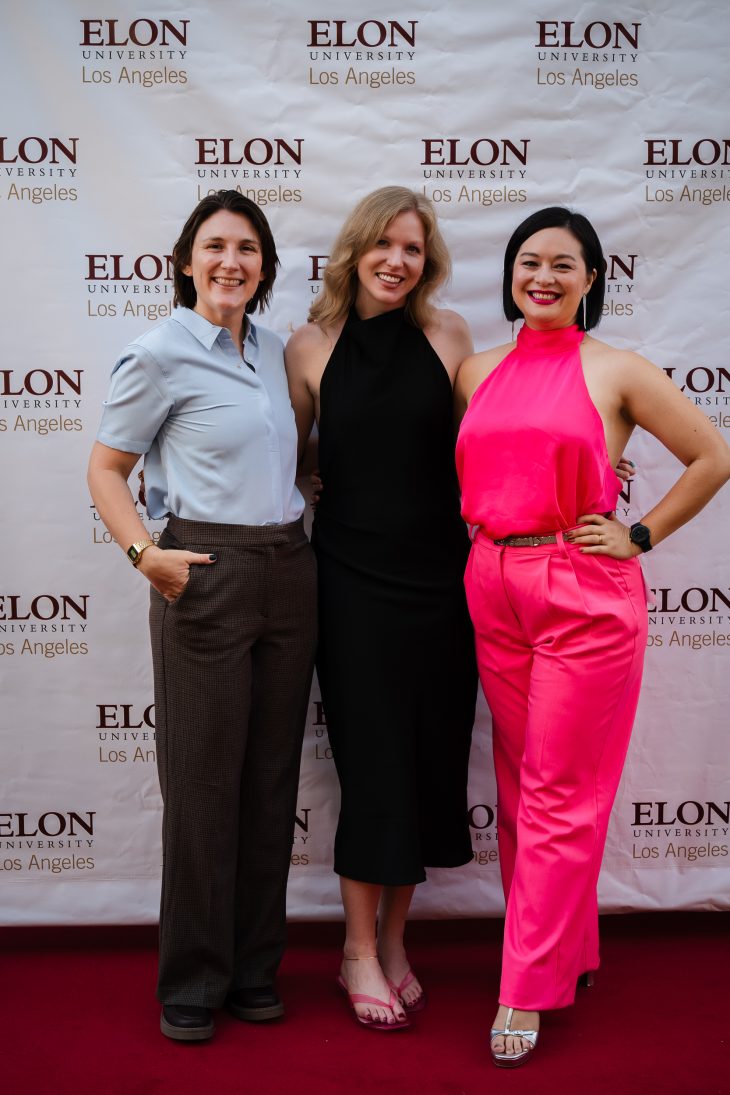 Three people pose for a photo on a red carpet in front of Elon signage