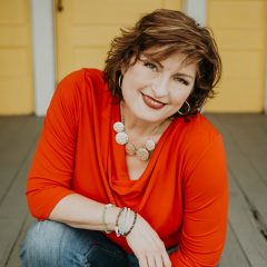 A woman smiling in a posed photo. She is wearing a red blouse and blue jeans.