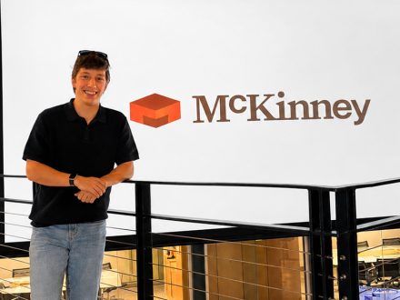 ���ϲ����� student stands in McKinney's contemporary office space.