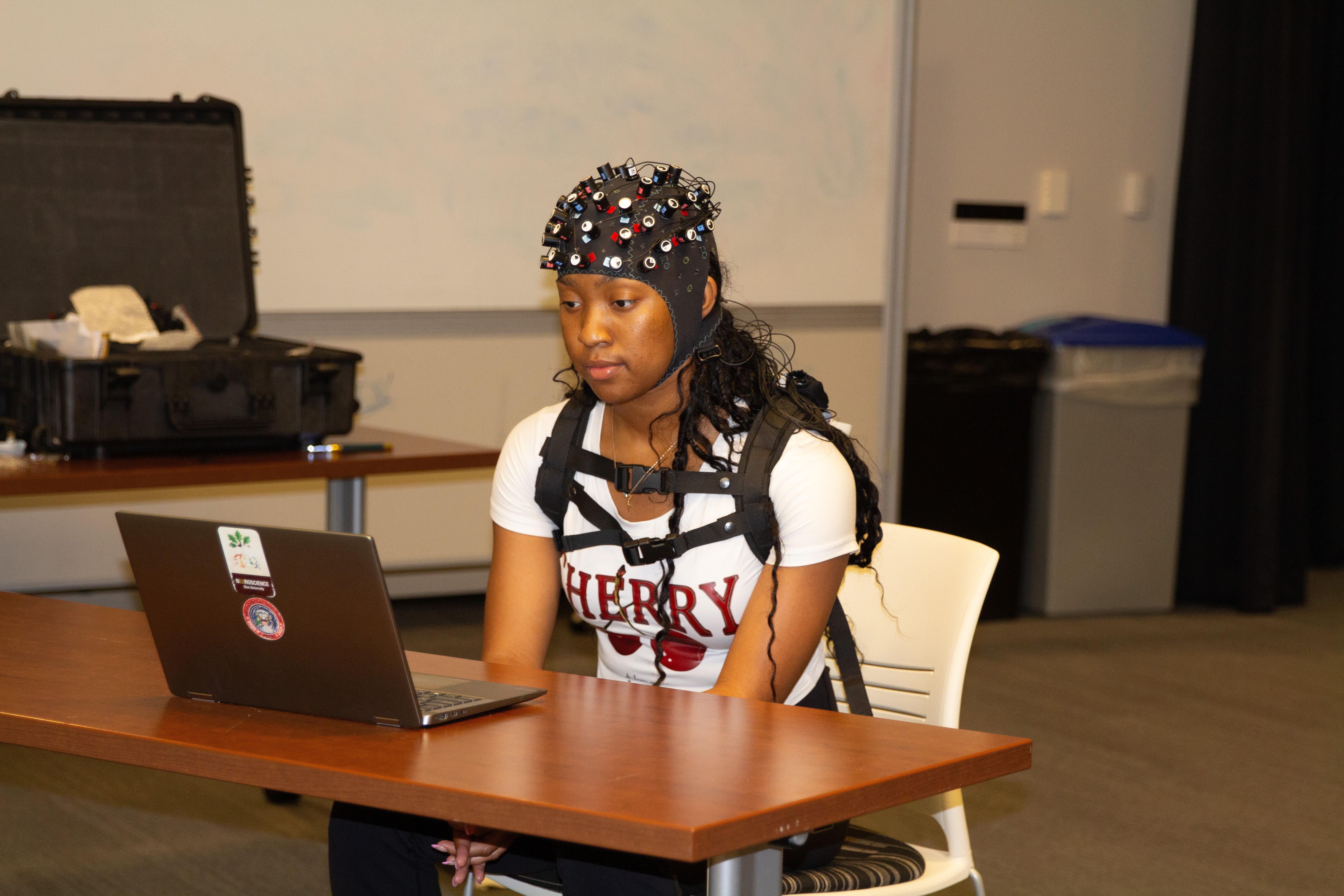 Student wearing a portable fNIRS device on her head while sitting in a chair looking at a computer.