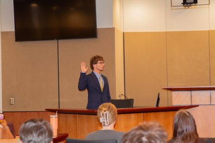 Student standing at a podium during a mock trial in the “Order in the court!, An introduction to law and justice” class