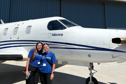 Jordan Green and fellow intern Daniela Pena stand in front of a white Labcorp aircraft outside a hangar.