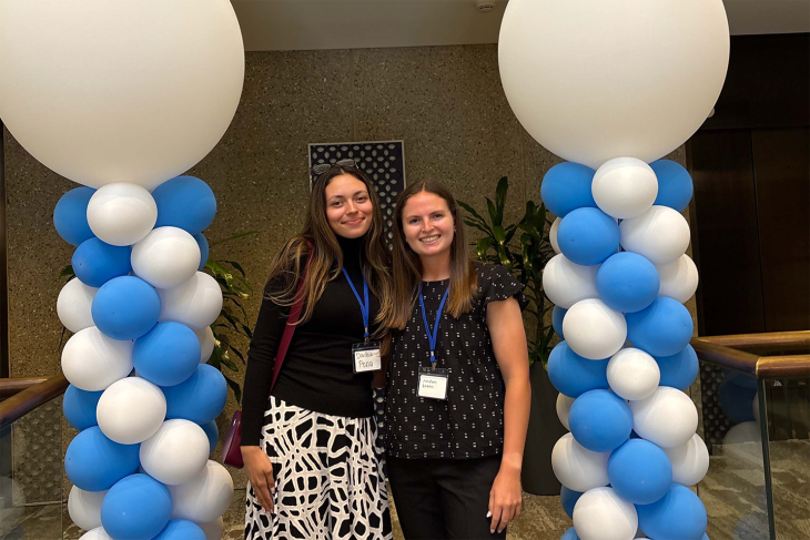 Jordan Green and fellow intern Daniela Pena stand together between two columns of blue and white balloons at a Labcorp event.