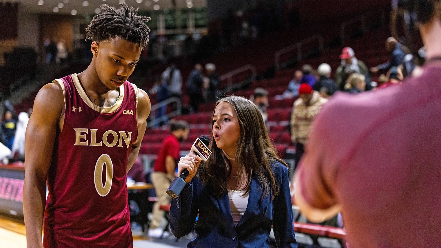 Rylee Marchand holds a microphone while talking to Elon basketball player