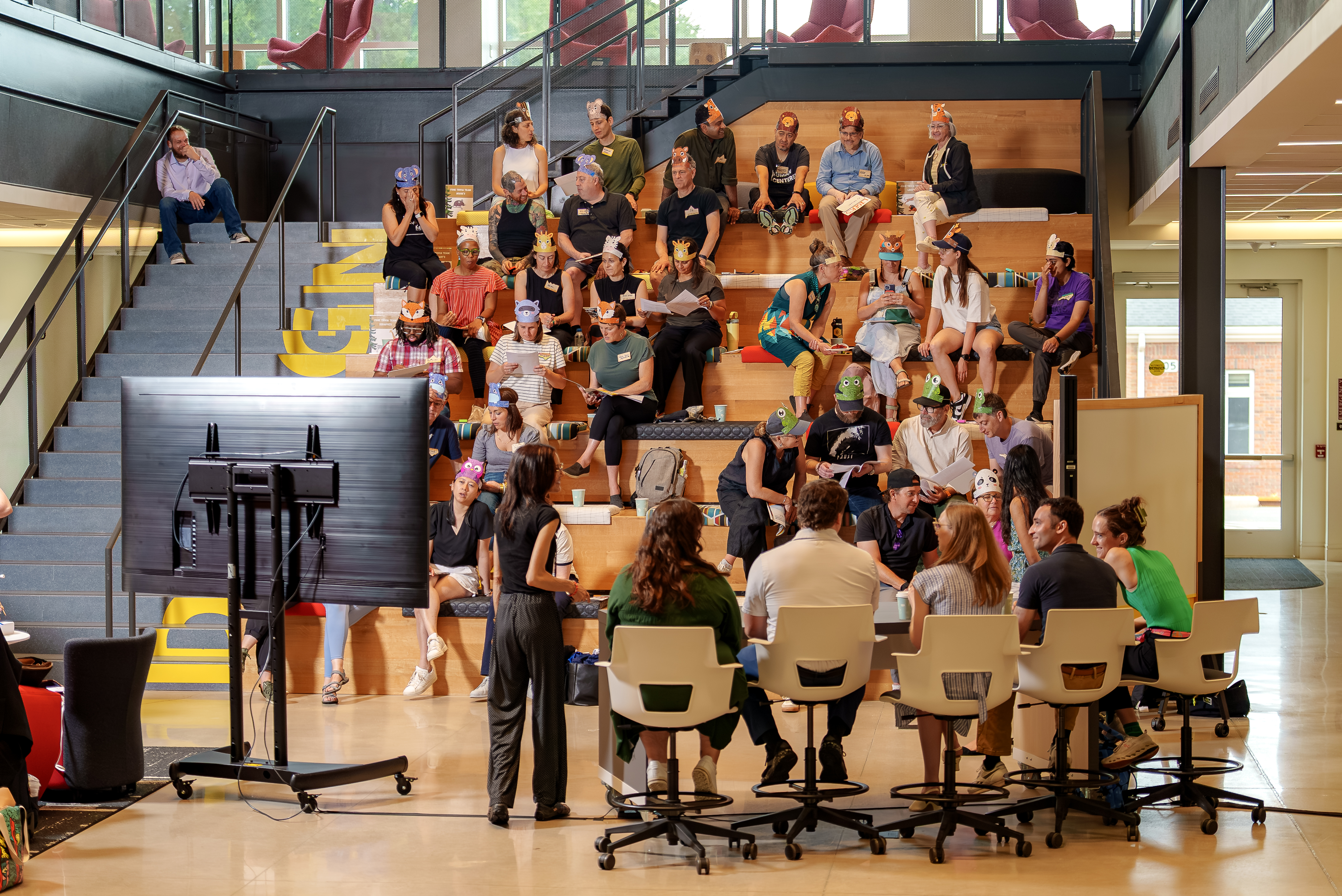 People gather on tiered seating inside Innovation Hall while a panel discussion takes place below, with attendees listening and participating in a collaborative campus event.