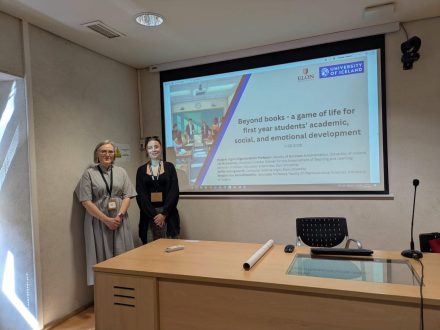 Two people stand next to a projector screen for a presentation