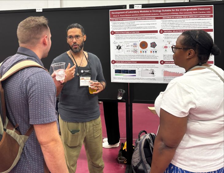 Three conference attendees stand in front of a research poster while its presenter gestures and explains the project. The poster, titled Development of Laboratory Modules in Virology Suitable for the Undergraduate Classroom, includes diagrams, charts and text describing undergraduate virology education and laboratory activities.