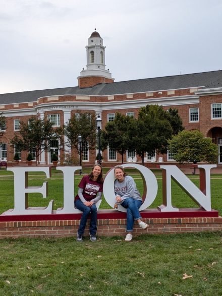 Kaitlin Henze ’12 and another woman sit on the large white ������Ƶ sign in front of the Inman ������Ƶ Welcome Center on ������Ƶ’s campus.
