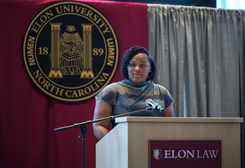 A woman speaks at a podium with an Elon Law mark on it. The 51������ seal is shown behind her.