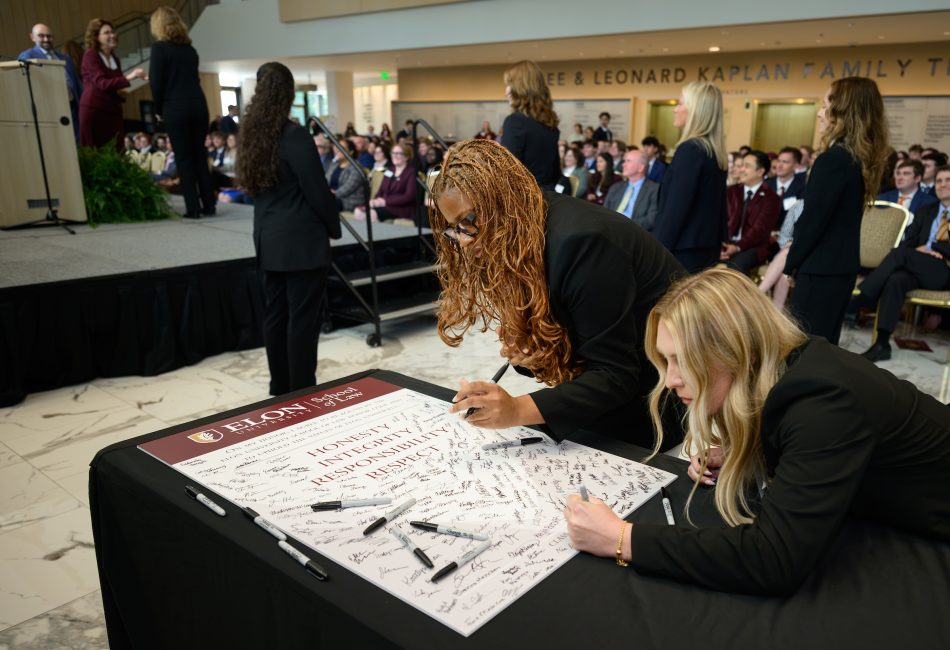 Two students leaning over a table signing a large white poster that says Honesty, Integrity, Responsibility and Respect.
