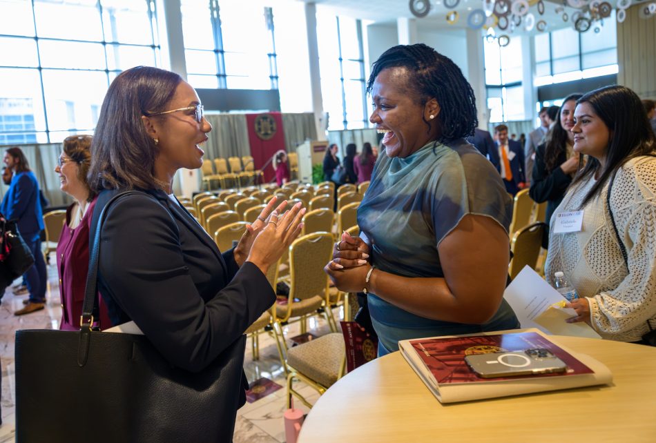 Two women smiling and laughing as they converse inside a theater atrium.