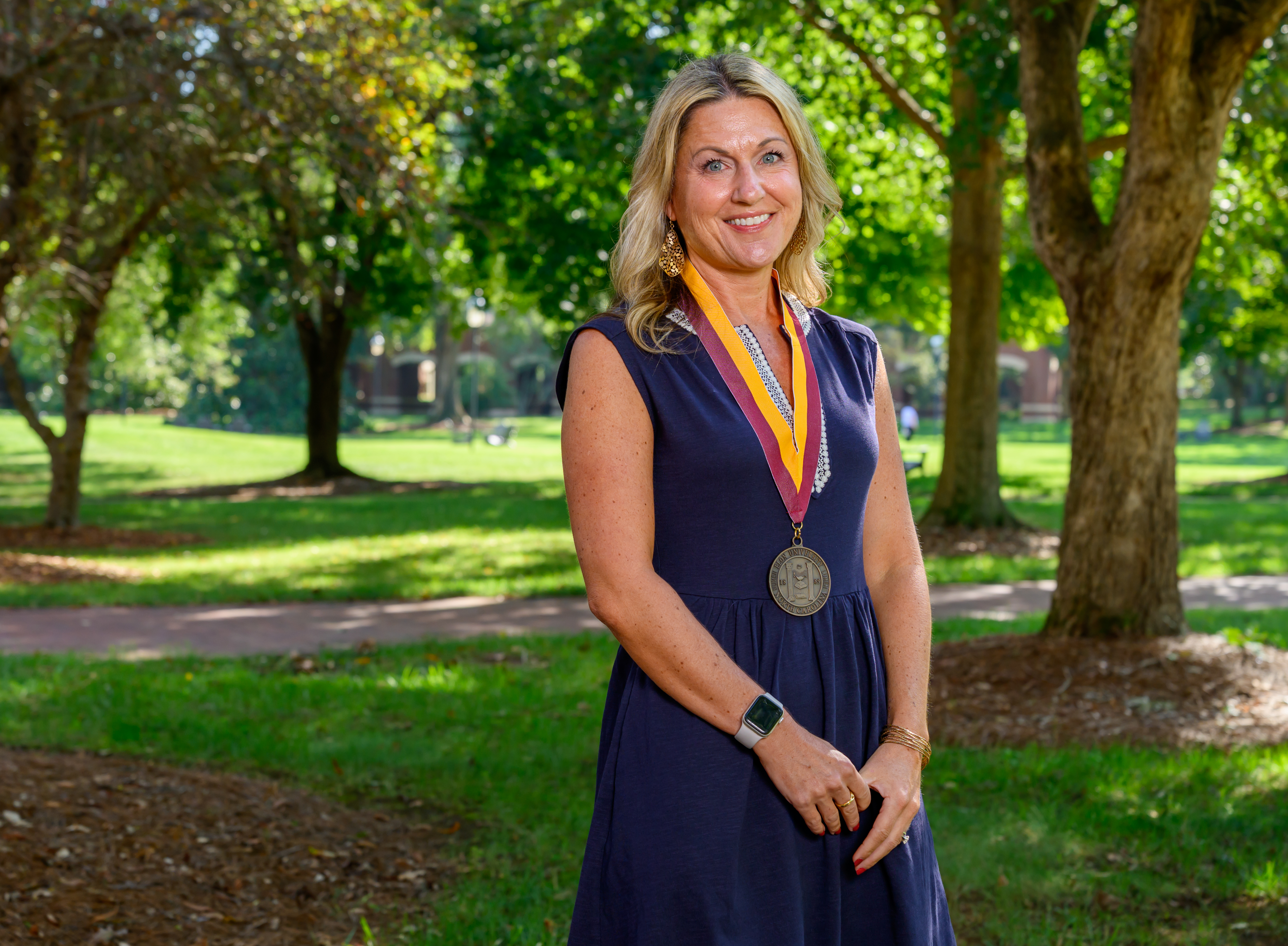 A woman stands in an outdoor setting wearing the Elon Medallion