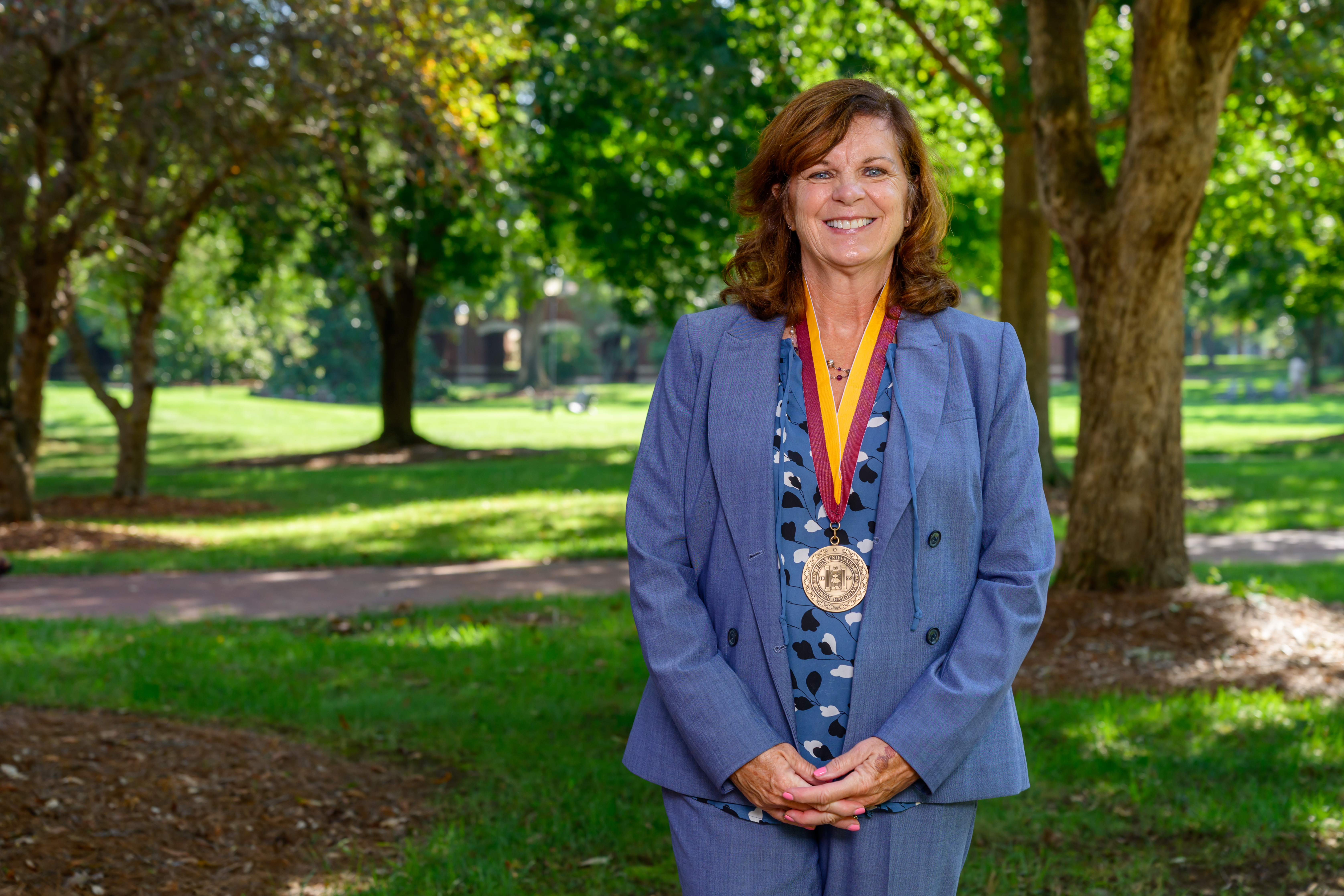 Mary Thornton smiles outdoors on Elon’s campus while wearing the Elon Medallion around her neck.