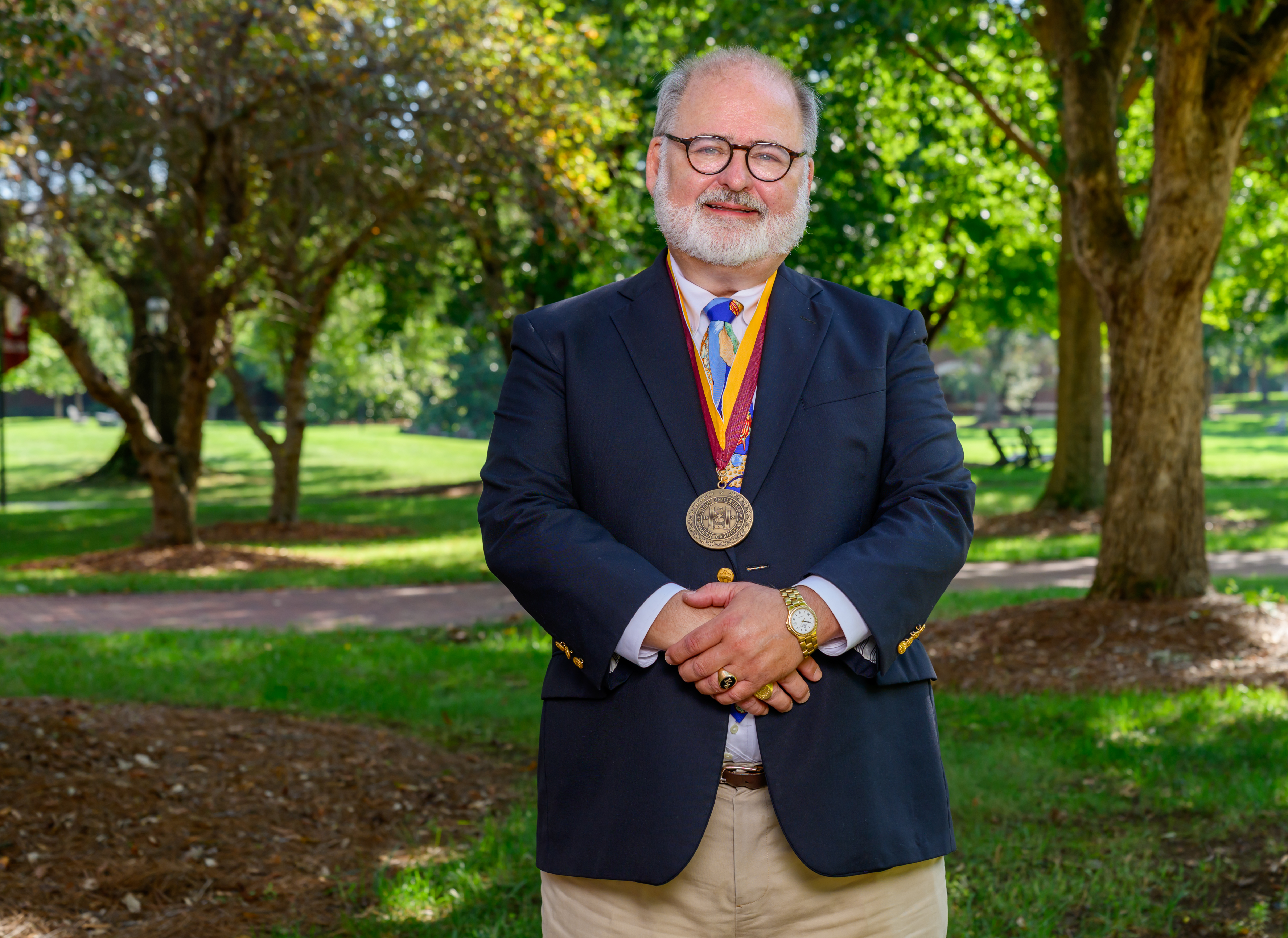  Jim Donathan poses outdoors on Elon’s campus wearing the Elon Medallion, a dark blazer and colorful tie.