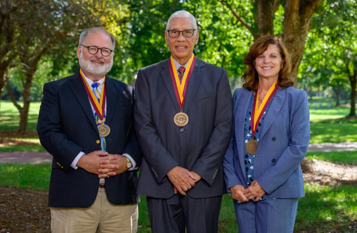 Three people pose for a photo wearing medallions in an outdoor setting
