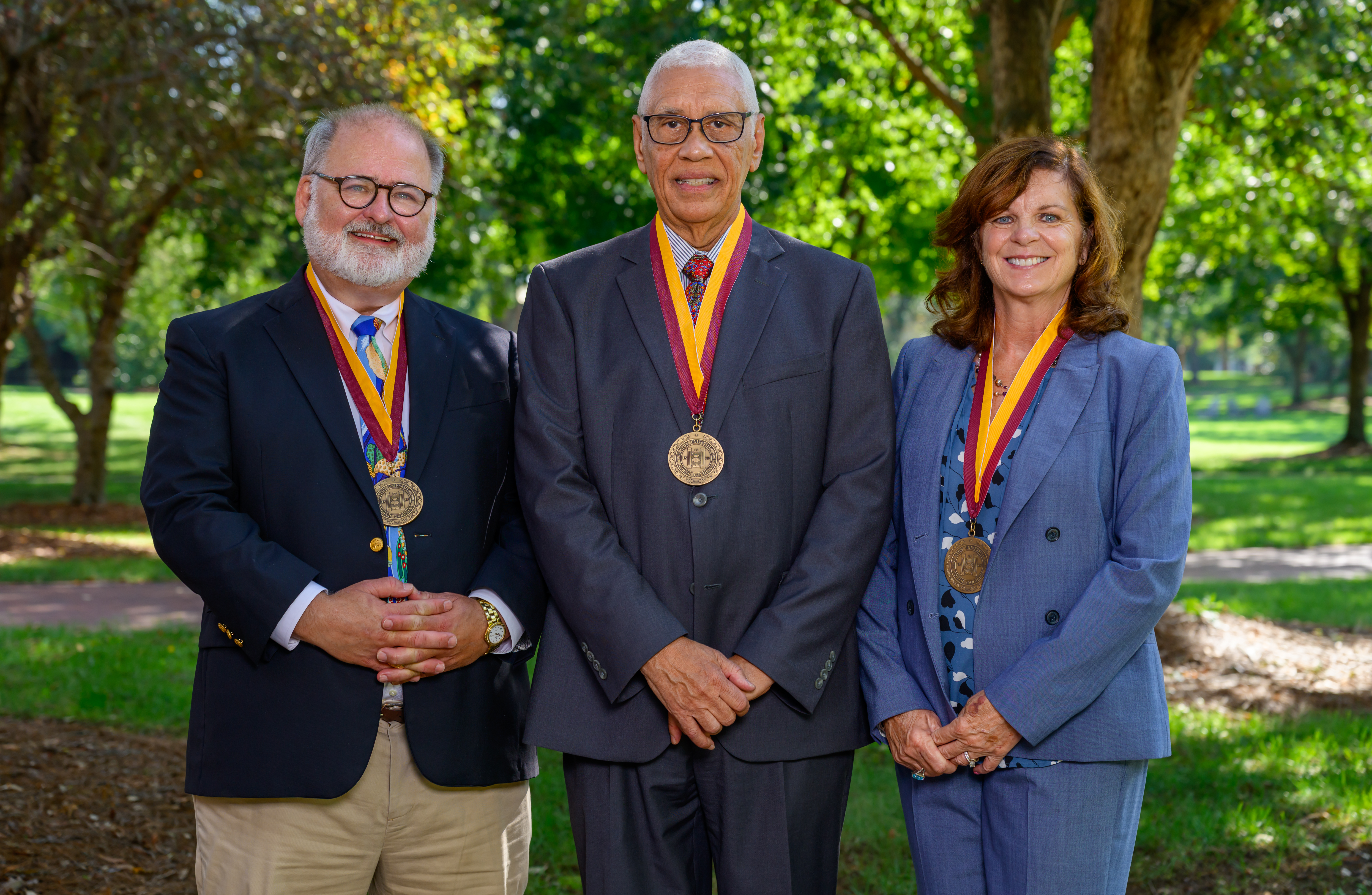 Three people pose for a photo wearing medallions in an outdoor setting
