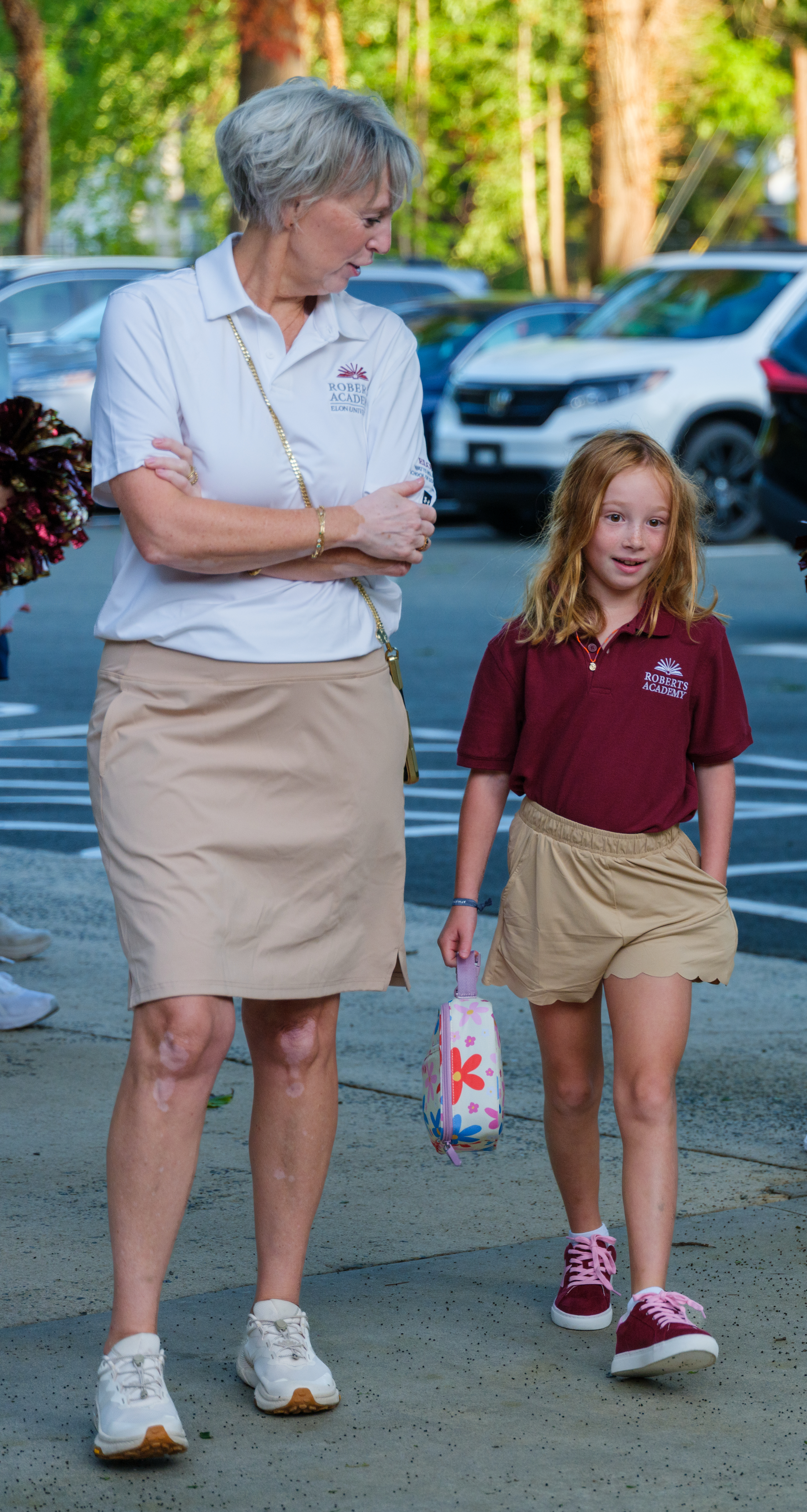A Roberts Academy student in a maroon school polo walks beside a staff member while arriving for the first day of school.
