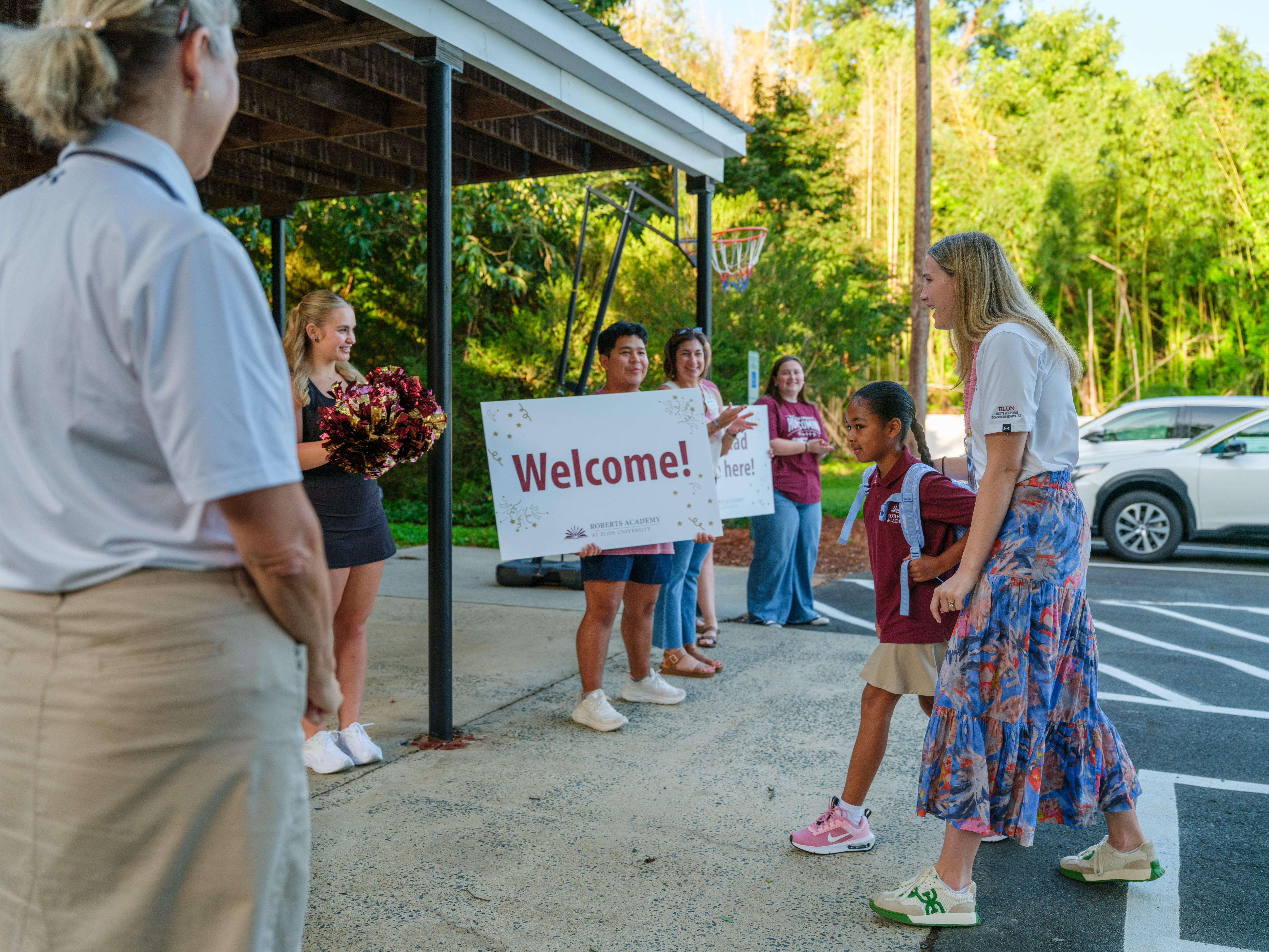 A Roberts Academy student and staff member walk toward the school while Elon employees applaud their arrival.