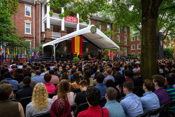 New students fill rows of chairs beneath the trees during New Student Convocation, with a “2030” banner displayed on West Residence Hall.