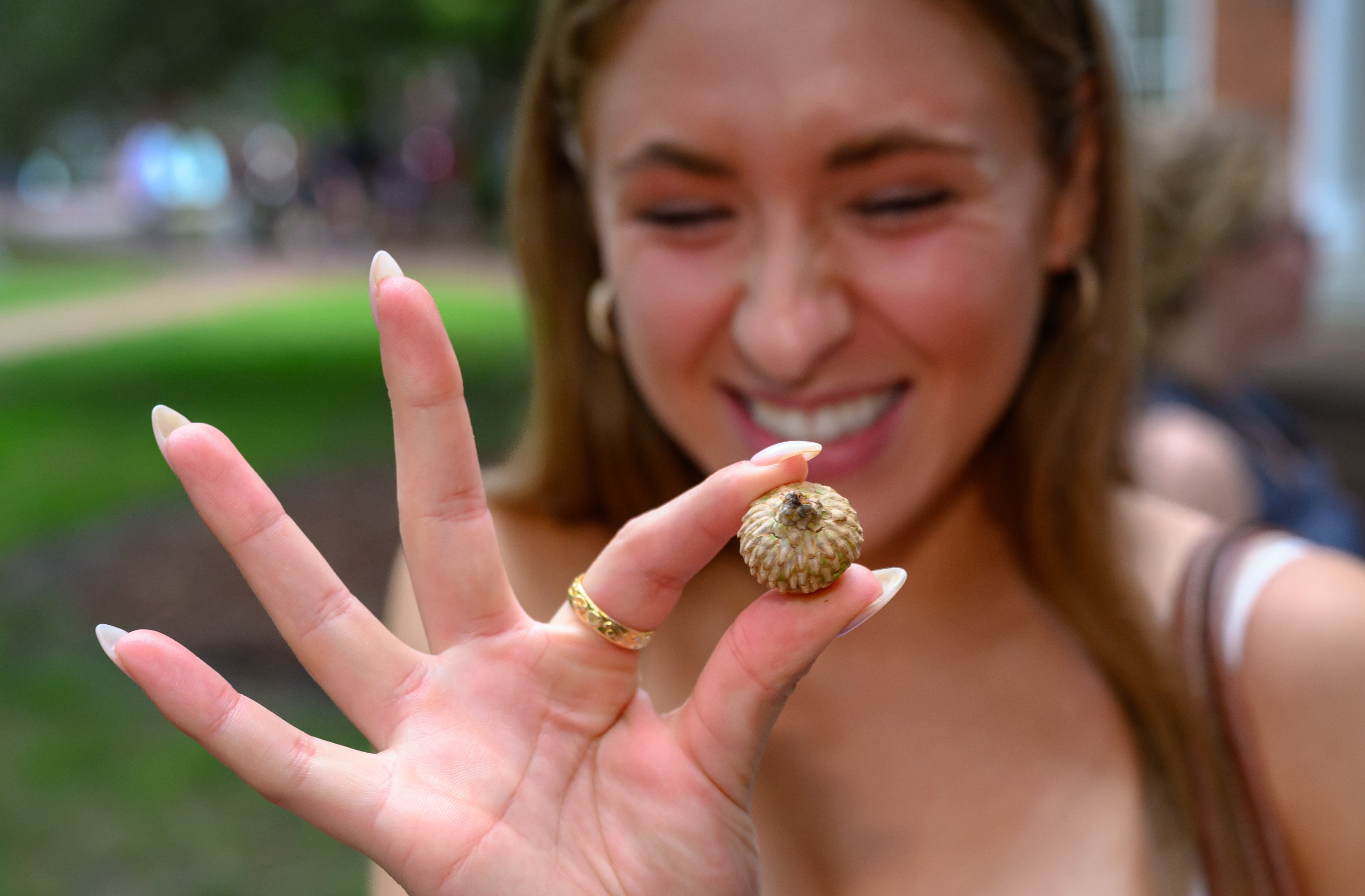 A smiling student holds a small acorn between her fingers during New Student Convocation.