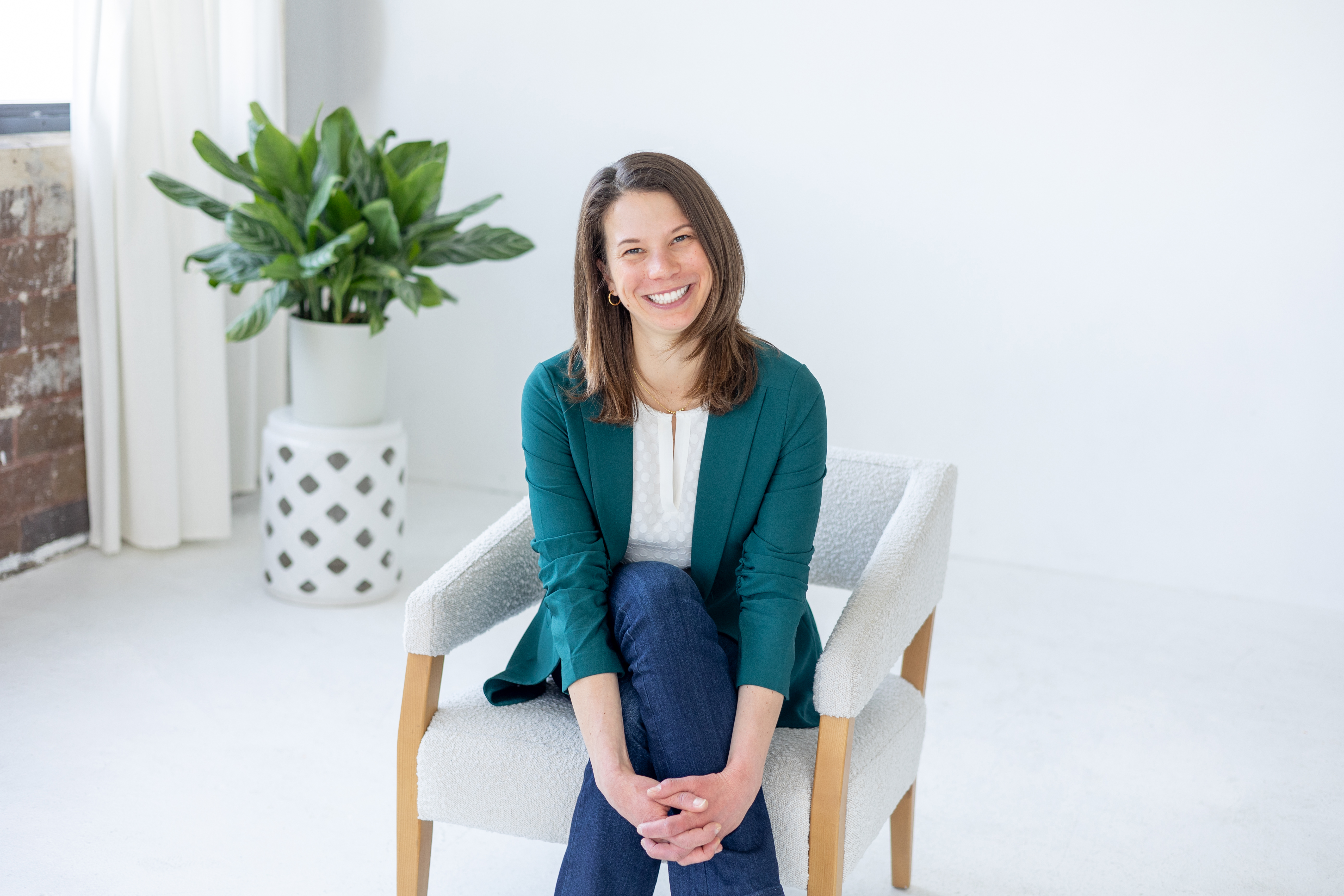 A woman smiles while seated in a chair during a professional portrait session in a bright studio.
